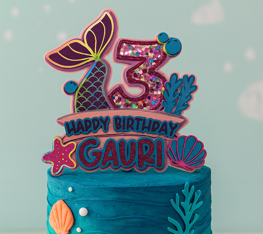 Blue birthday cake with decorative topper featuring 'Happy Birthday' on a light blue background